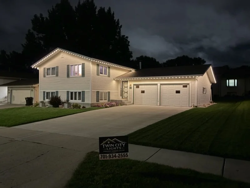 Two-story home with LED soffit lighting along roofline and gable edges, illuminating cream siding and garage