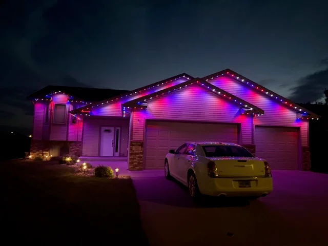 Home exterior with magenta and purple LED accent lighting on roofline, soffits, and garage door