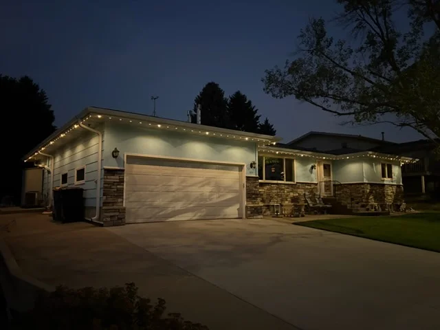 Home exterior with LED soffit lighting, stone veneer accent lights, and illuminated garage door at dusk