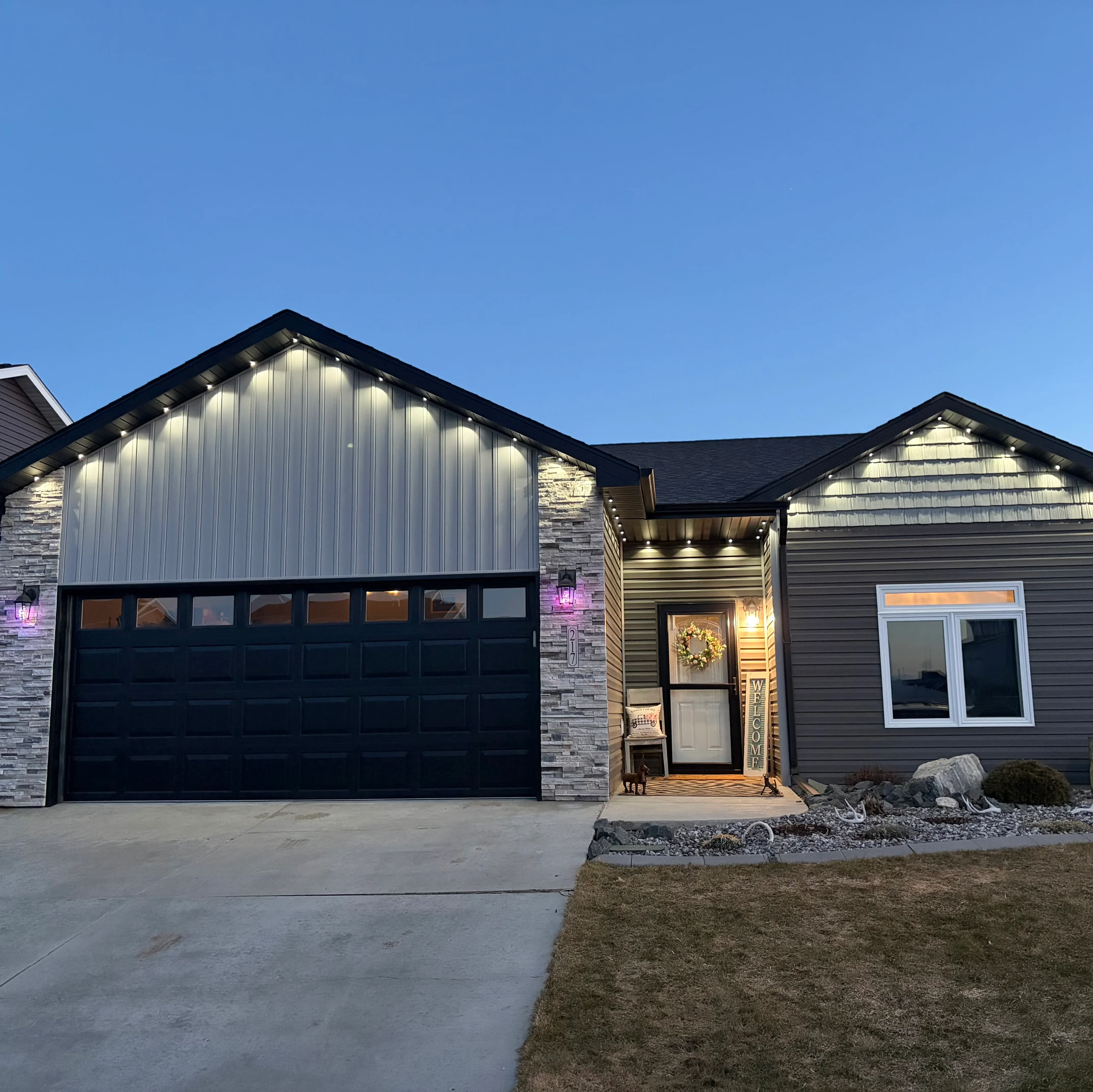 Modern home exterior with recessed soffit lights, stone pillar uplighting, and entry accent lighting at dusk